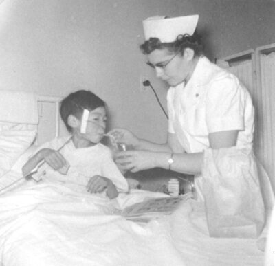 A nurse holds a cup with a straw to a boy's mouth. The boy has a tube in his nose that is taped to the side of his head.