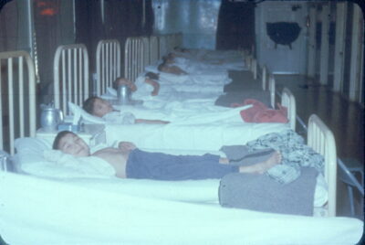 A row of boys lying in hospital beds.