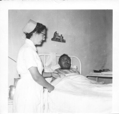 A nurse tucks a man into a hospital bed.