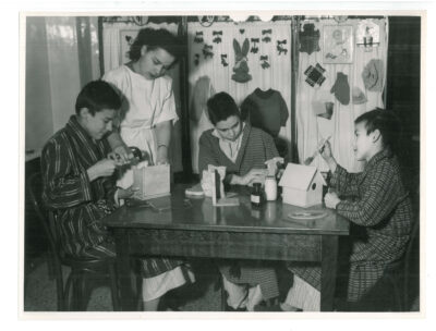 Three boy patients making birdhouses. A nurse helps one of the boys with a hammer.