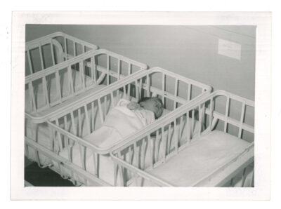 Baby in crib next to three empty cribs
