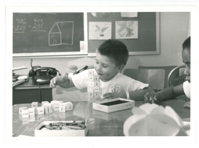 Boy in classroom playing with word blocks. Another boy can be seen at the edge of the photo