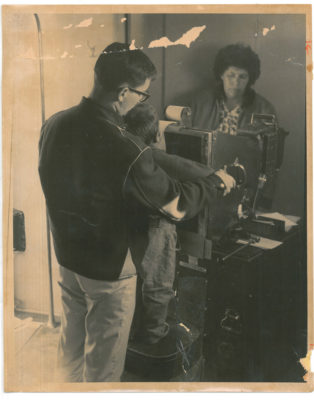 Man holding a boy in front of a machine and woman stands on other side of machine