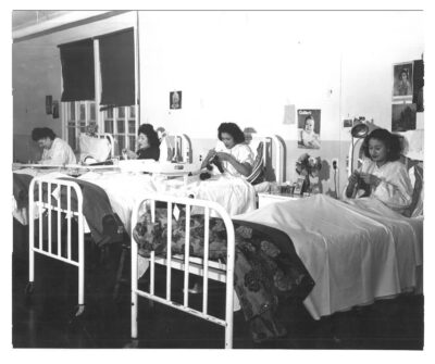 Four women in hospital beds knitting.