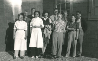 A group of men and women standing outside next to a building.