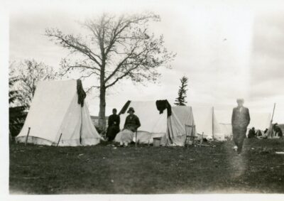 Group of small tents. Two women sit in between the tents, and a man walks nearby.
