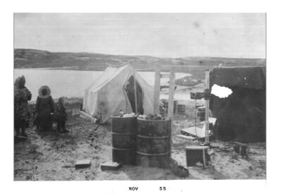 Traveling clinic; A camp next to a body of water with a tent and a portable x-ray machine. People in parkas can be seen around the camp.
