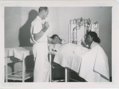 A woman lies on a hospital bed while a man performes a medical procedure on her abdomen. A nurse operates a machine next to the bed.