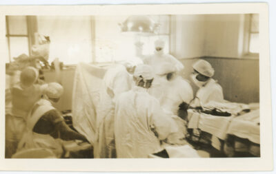 Doctors and nurses conducting a procedure in an operating room. The patient is obscured from view.