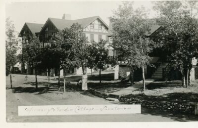 Exterior view of two buildings with trees in front. A nurse stands between the two buildings. An inscription reads, "Infirmary & Gordon Cottage - Sanatorium"