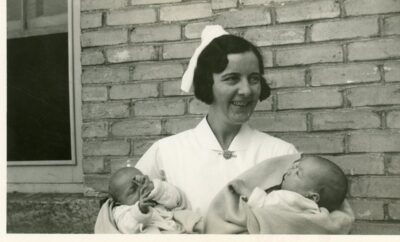 A nurse stands outside of a building holding two babies.