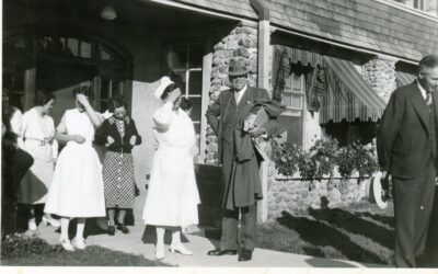 A group of nurses and two men stand outside the entrance of a building.