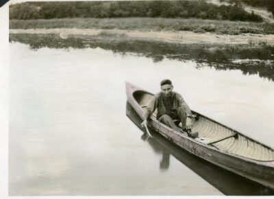 A man in a canoe on a body of water. From album page MBLung-11-14-001