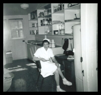 A nurse sits at a desk. Jars and cans sit on the shelves above her.