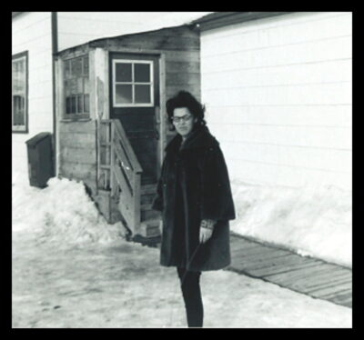 A woman in a fur coat stands outside next to a building.