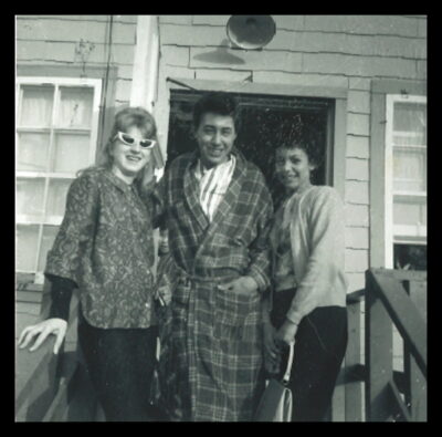Two women and a man in a plaid robe stand at the entrance of a building.
