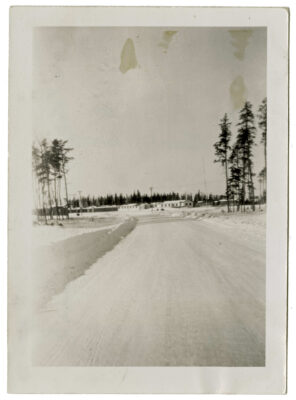 A snowy road leading up to the Clearwater Lake Indian Hospital. Some trees (tall and sparse) stand on either side of the road.