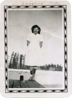 A woman in a white nurse's outfit stands on a dock. The photo has a patterend border around the edge.