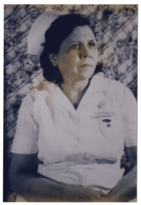A portrait of a woman in a nursing uniform complete with nurse's cap.  Over her left breast pocket she wears a name tag. On the pocket is a label that reads "SAH" (St. Anthony's Hospital).